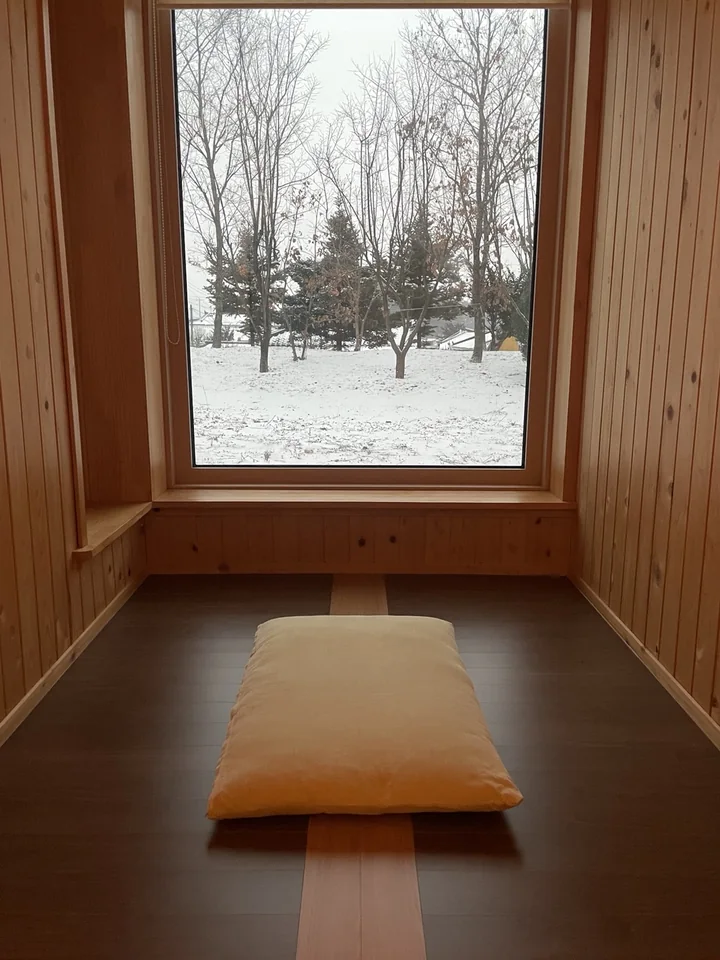 A meditation cushion beside a window overlooking a snowy garden